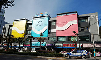 도로 건너편에서 바라본 노란색이 눈에띄는 ㈜중앙시장건물의 외부전경과 1층에 들어선 다양한 상가들