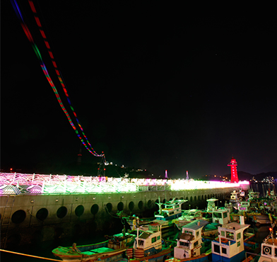 海洋公園に停泊している船舶とバンパジェの末に赤く輝いているハメル灯台、その上を通過する色とりどりのケーブルカー