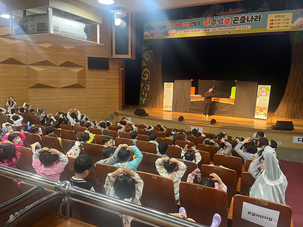 어린이들이 공연을 관람하며 즐거운 시간을 보내고 있는 모습으로, 무대에서는 공연자가 활동하고 있다.