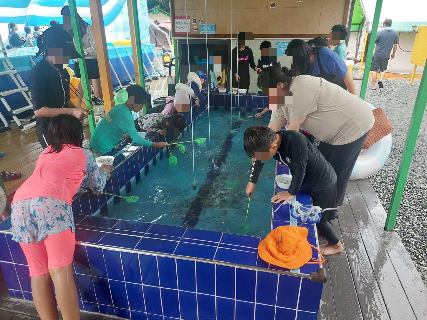 어린이들이 수조에서 물고기를 잡으려고 노력하고 있는 장면이다. 몇몇 성인이 아이들을 도와주고 있다.