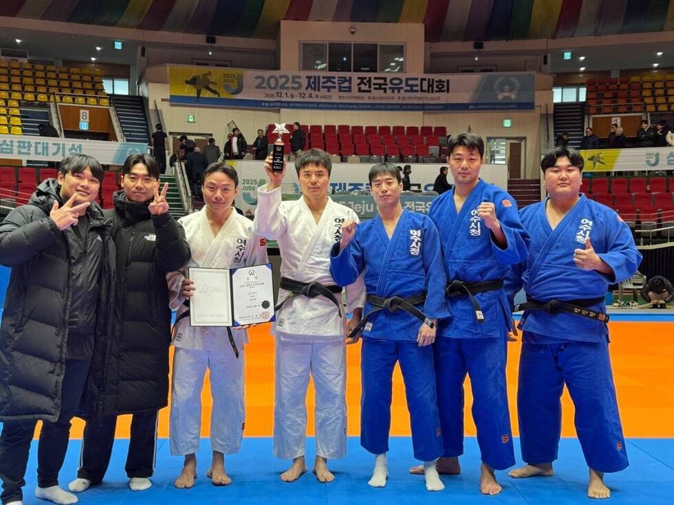 실내 유도 경기장에서 여수시청 유도팀 선수들과 코치진이 함께 포즈를 취하고 있으며, 선수들은 유도복을 입고 상장과 트로피를 들고 서 있고 뒤편에는 ‘2025 제주컵 전국유도대회’ 현수막이 걸린 관중석과 경기장이 보이는 모습.
